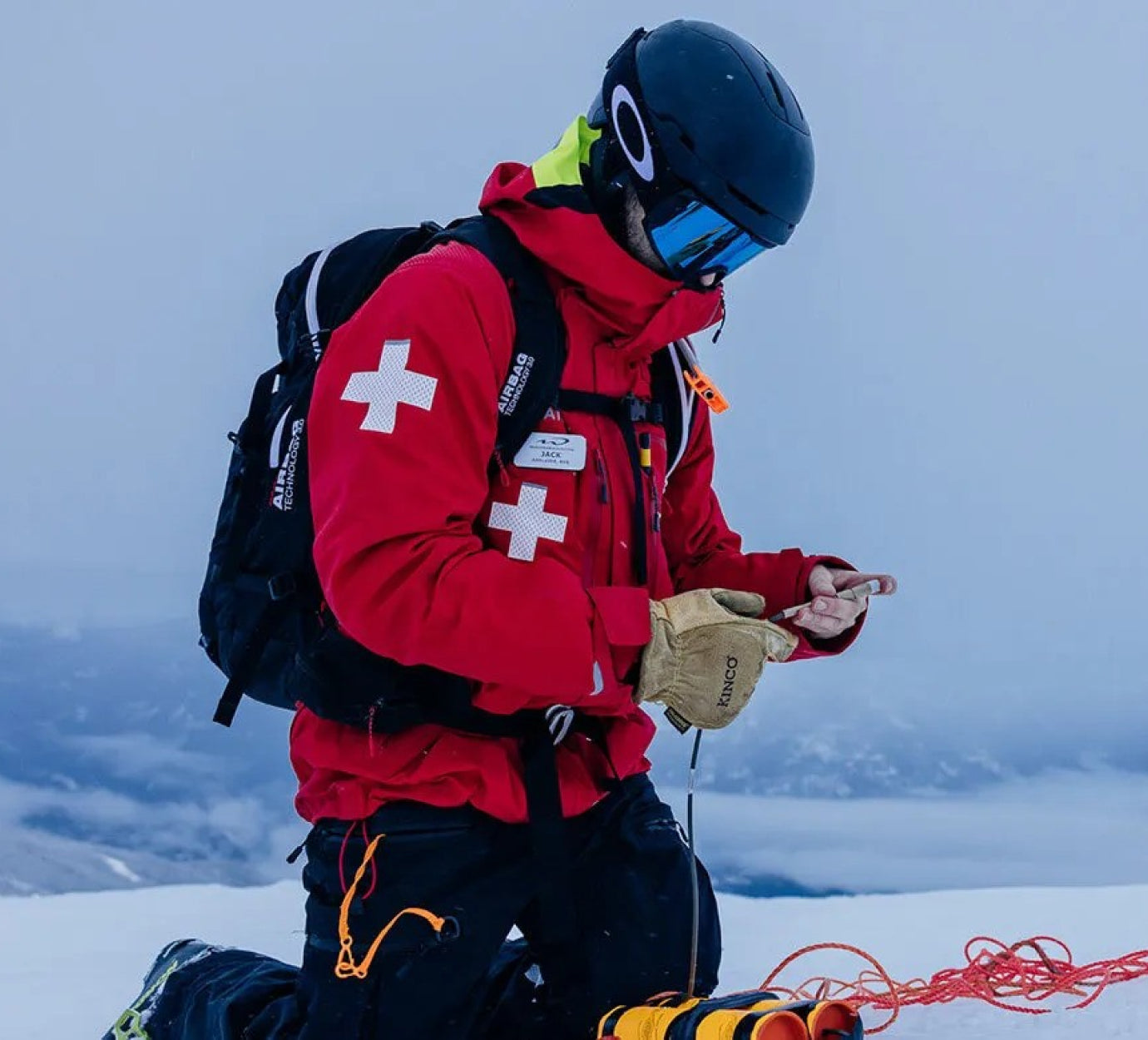 National Ski Patrol member kneeling in the snow, handling cables and ropes during a rescue or training operation