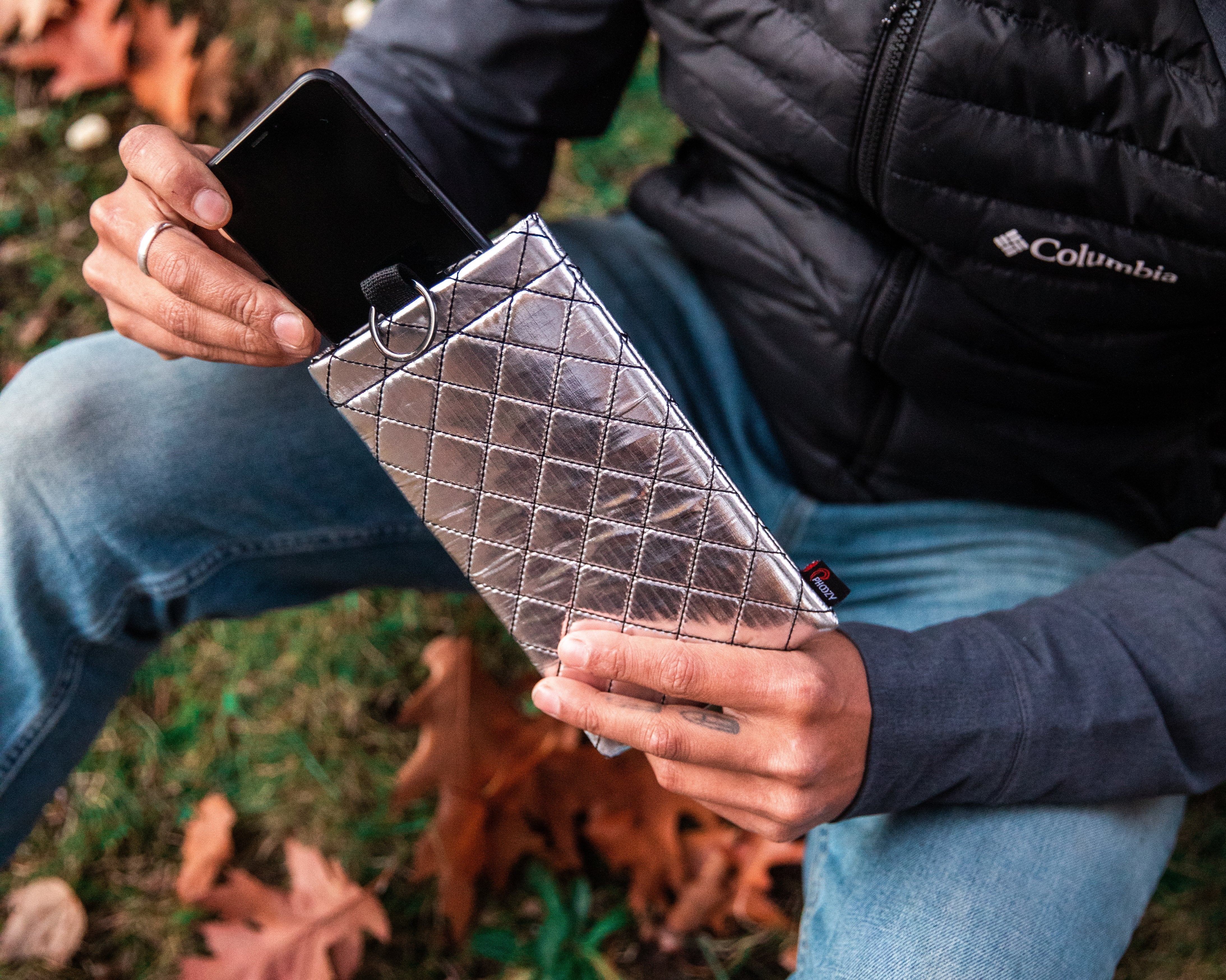 Man sitting outdoors in fall leaves removing his smartphone from a PHOOZY Thermal Phone Capsule in cold weather.
